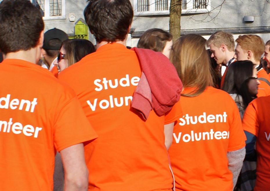 A group of students in bright orange t-shirt which say 'Student Volunteer' on them gather in central Oxford