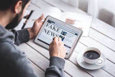 man working o ipad with words fake news on screen