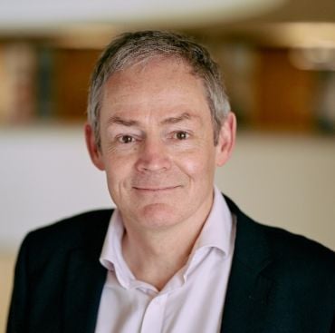 Professor Dominic O’Brien, a middle aged white man wearing a black suit and white shirt.