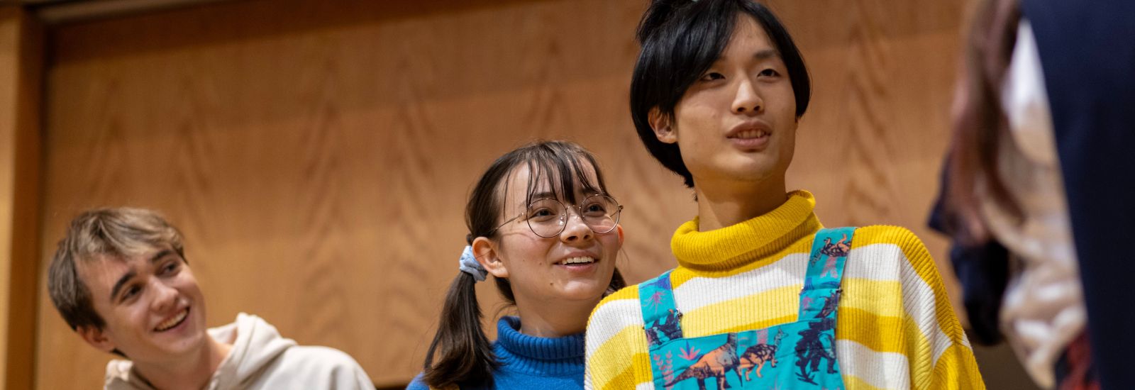 Three students look to their left, smiling and laughing, whilst acting in an amateur dramatic performance.