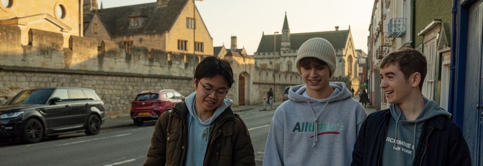 Three students walk along an Oxford street, laughing as they speak to one another.