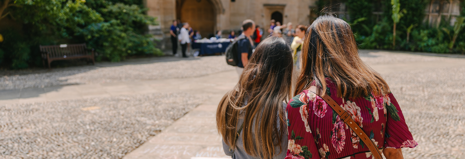 Two Open Day visitors look out across a college courtyard, with ambassadors and other visitors talking in the background. 
