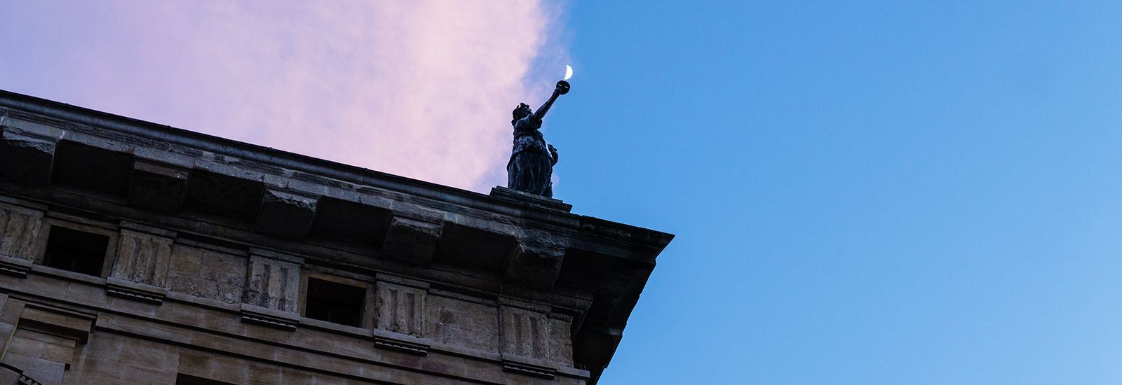 A statue on the corner of the Clarendon Building at dusk