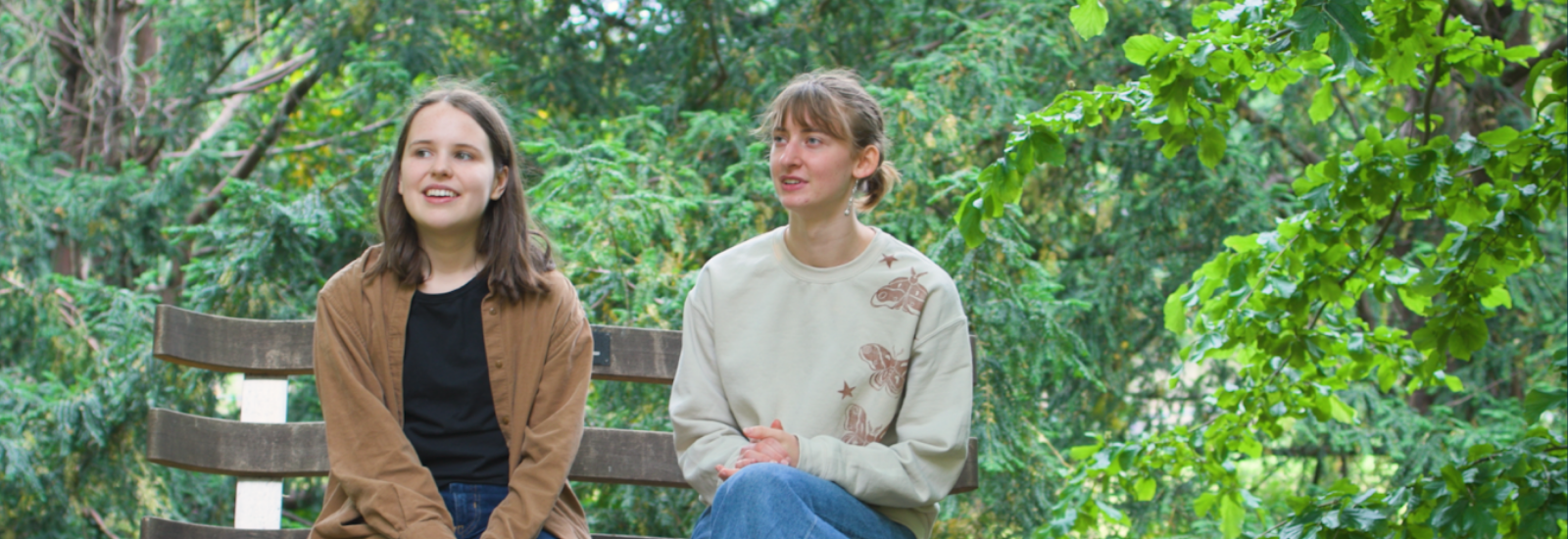 two students sitting on a bench with trees in background