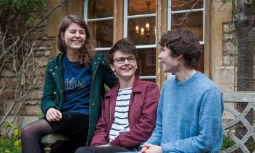 Three students sat on a bench chatting between lectures