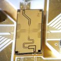A rectangular quantum computing chip against a circuit board background.